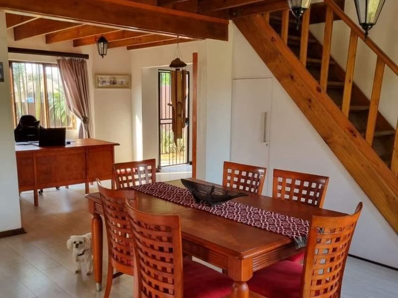Open-plan living and dining area featuring exposed timber ceiling beams, a wooden staircase, and laminate flooring, creating a warm and inviting atmosphere.