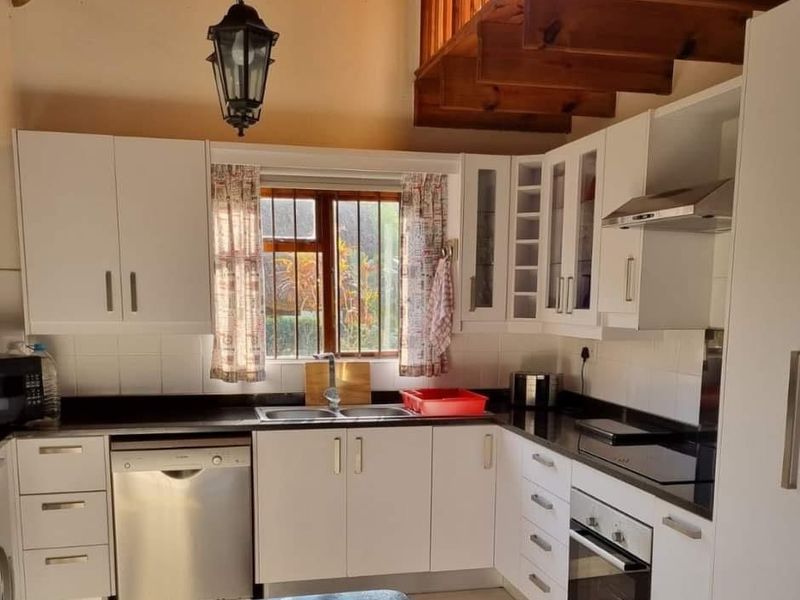 A functional kitchen featuring white cabinetry, black granite countertops, built-in oven, extractor fan, and a wooden staircase leading to an upper level.