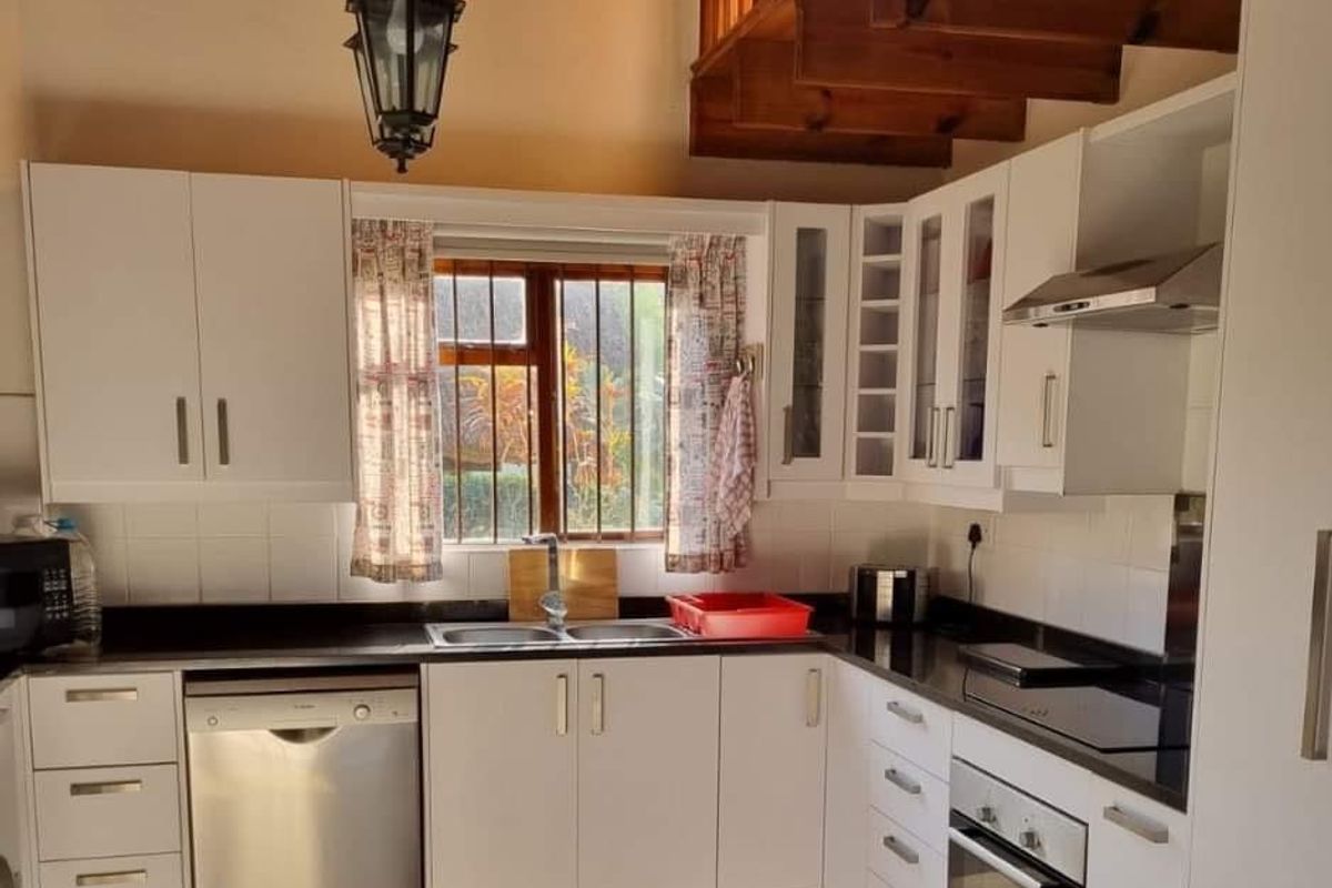 A functional kitchen featuring white cabinetry, black granite countertops, built-in oven, extractor fan, and a wooden staircase leading to an upper level.