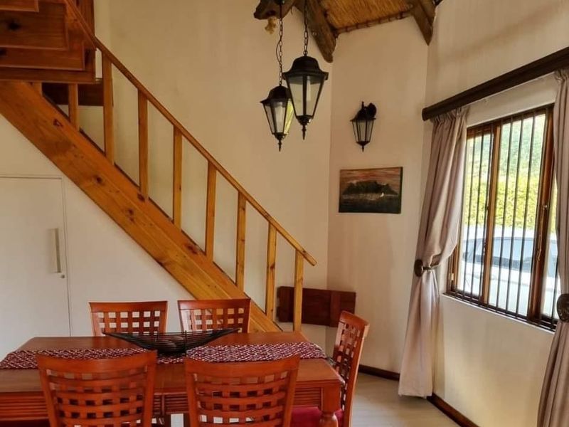 Dining area featuring a wooden staircase, exposed thatched ceiling, and traditional pendant lighting, with security bars installed on the window.