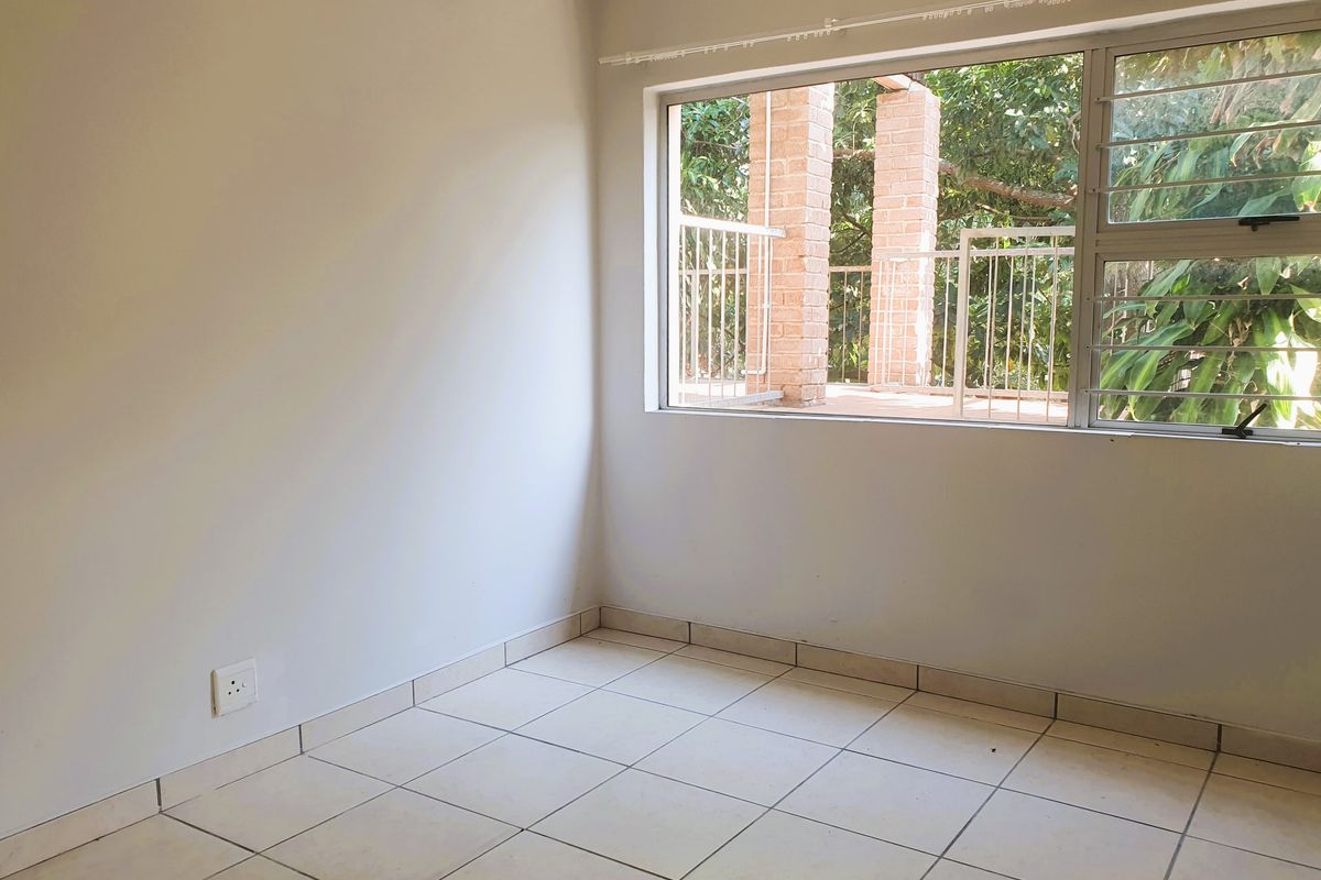 A vacant bedroom featuring neutral tiled flooring, large aluminium-framed windows with security bars, and a clean, blank canvas ready for personalization.