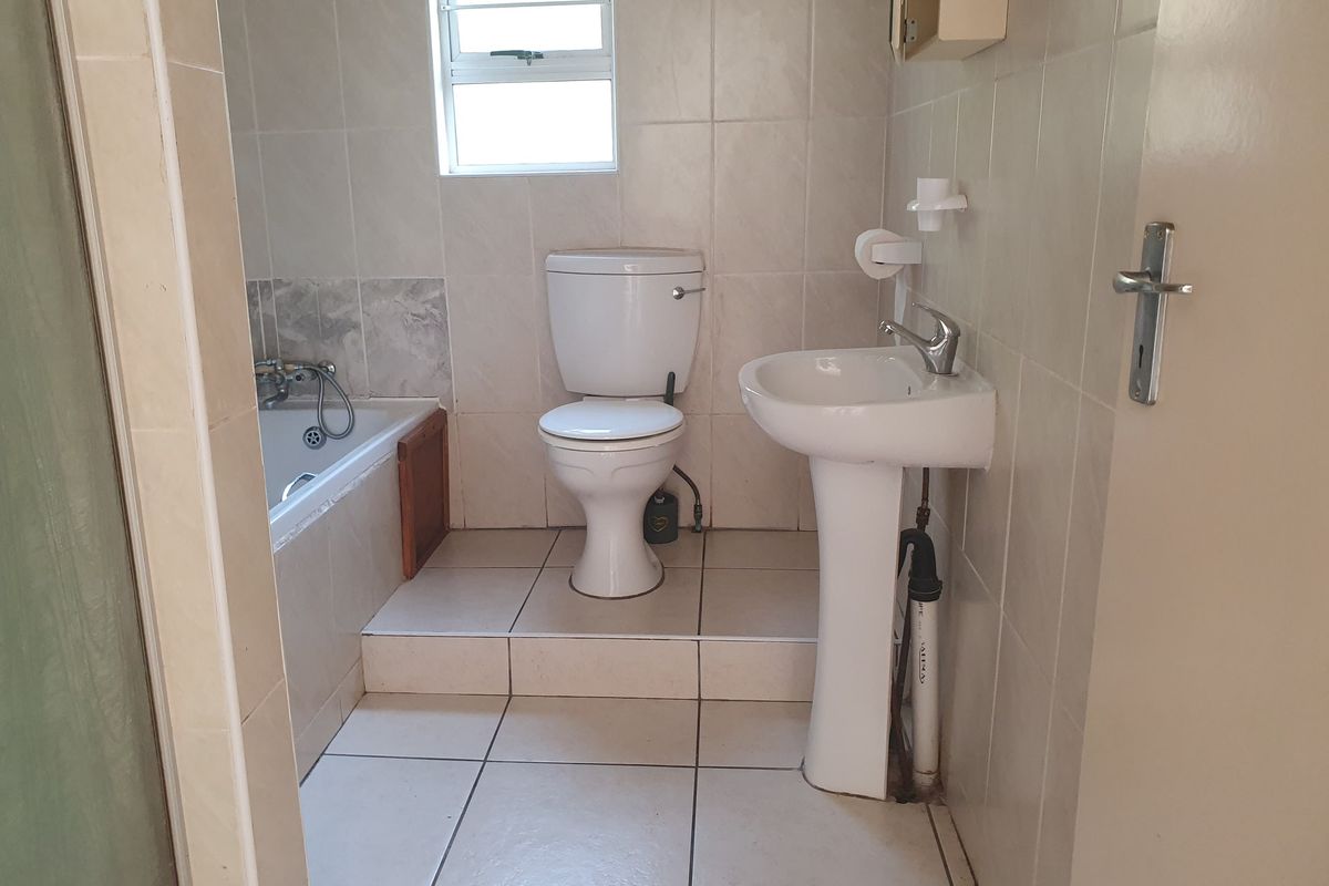 A functional bathroom featuring a pedestal basin, toilet, and bathtub with neutral wall and floor tiling.