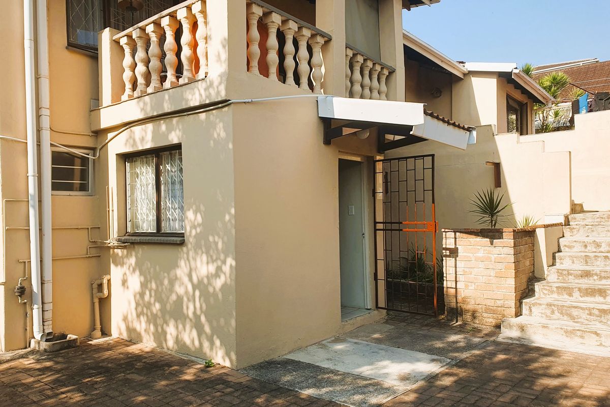 Rear exterior view of the property featuring a balcony with balustrades, brick staircase, and paved courtyard area.