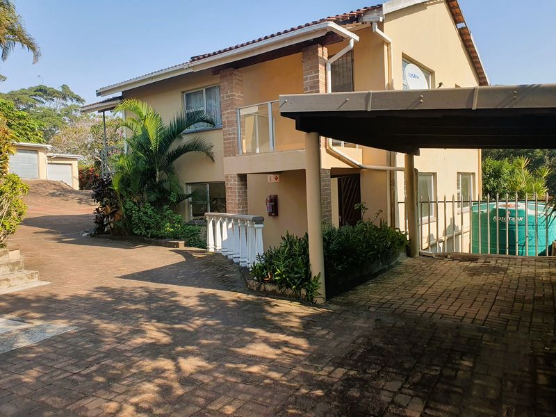 Front exterior view of a double-story house featuring a paved driveway, carport, and balcony with balustrade.