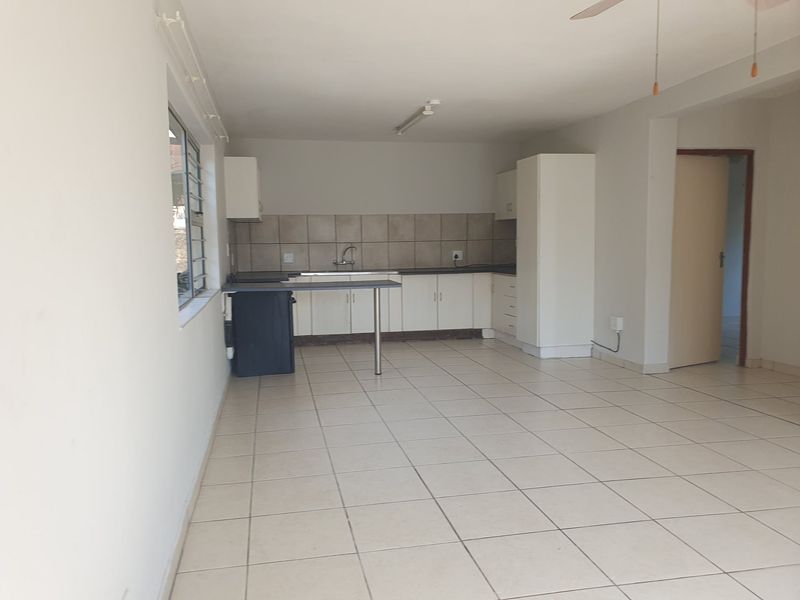 An open-plan living and kitchen area featuring tiled flooring, built-in cabinetry, and a functional kitchen layout, offering a blank canvas for renovation.