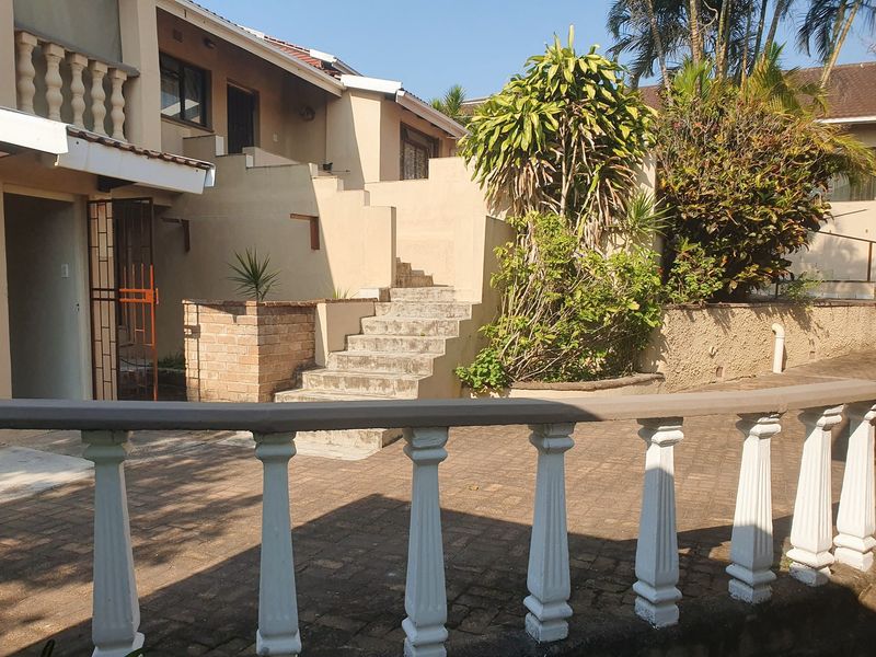 Rear exterior view of the property featuring a paved courtyard, concrete staircase, and traditional balustrade detailing.