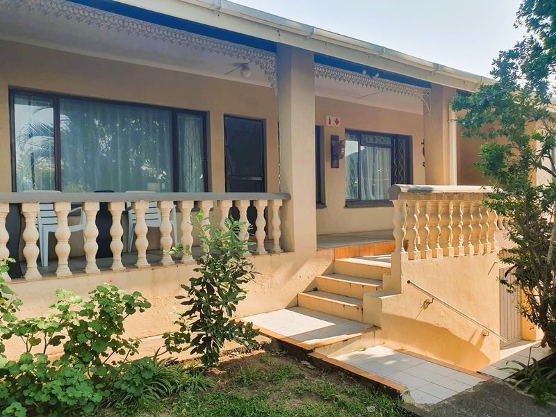 A covered patio area featuring classic balustrades, decorative fretwork, and tiled steps leading to the entrance.