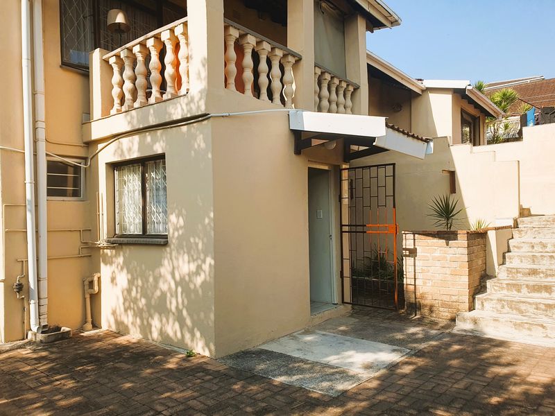 Rear exterior view of the property featuring a balcony with balustrades, brick staircase, and paved courtyard area.