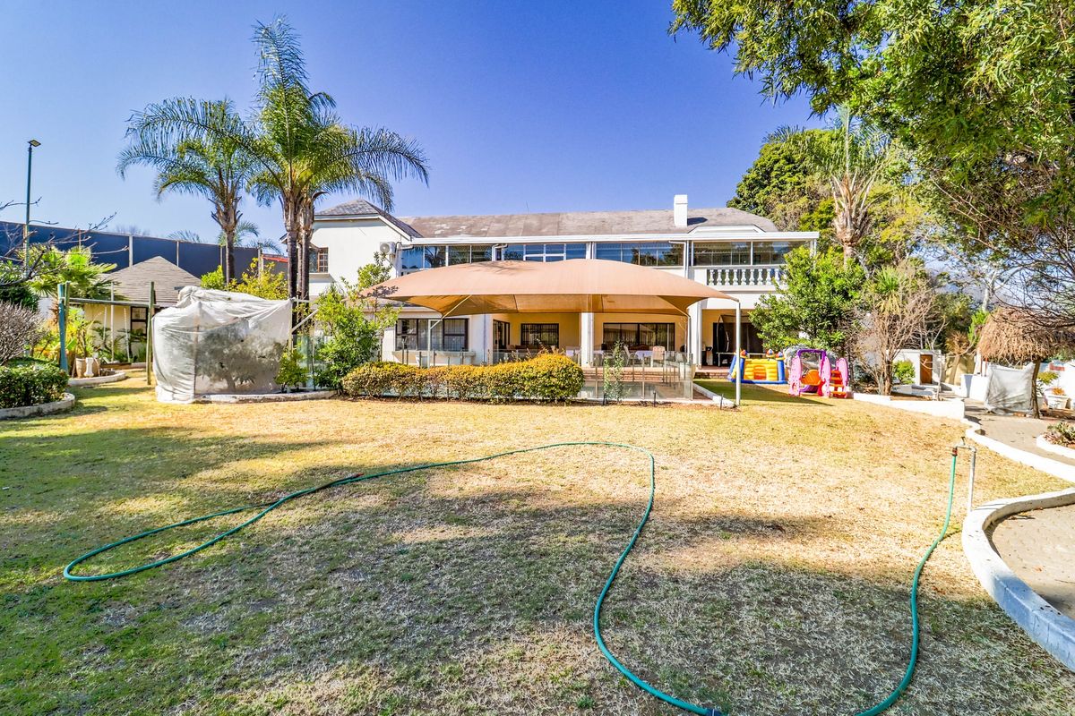 Rear view of the property featuring a spacious garden, a paved patio area with a large shade sail, and a balcony on the upper level.