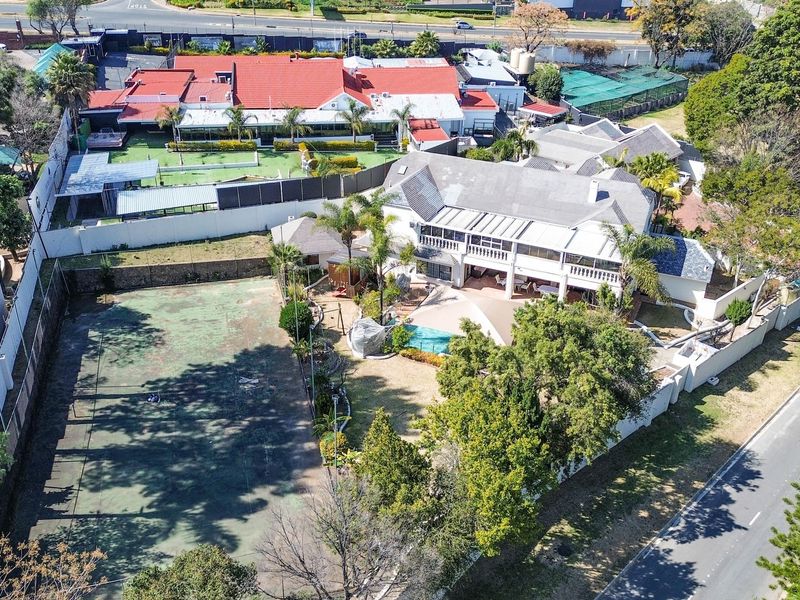 Aerial view of a residential property featuring a private tennis court, swimming pool, expansive patio, and multi-level dwelling with a tiled roof.