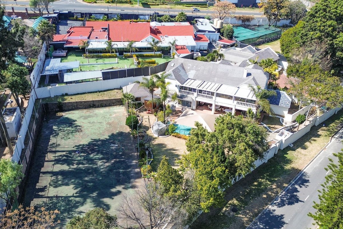 Aerial view of a residential property featuring a private tennis court, swimming pool, expansive patio, and multi-level dwelling with a tiled roof.