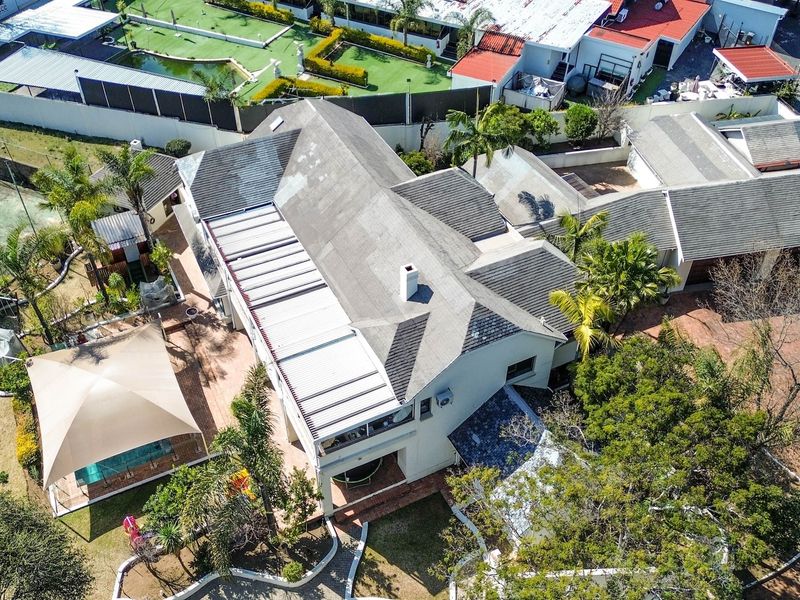 Aerial view of the property showcasing the main house, tiled roof, swimming pool, paved driveway, and surrounding garden area.