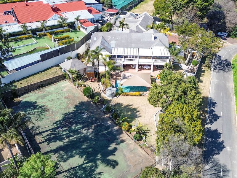 Aerial view of a residential property featuring a swimming pool, tennis court, and spacious outdoor patio areas set within a landscaped garden.
