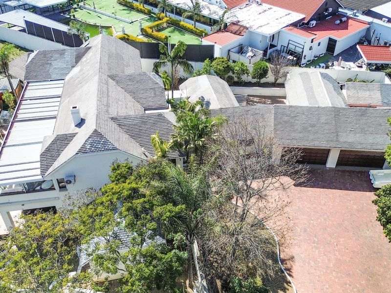Aerial view of the property showcasing the expansive tiled roof, paved driveway, double garage, and surrounding garden area with a swimming pool.