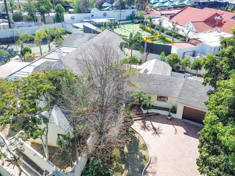 Aerial view of the property showcasing the tiled roof, paved driveway, double garage, and established garden surroundings.