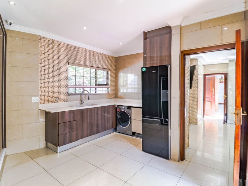A modern, well-maintained scullery featuring sleek dark wood cabinetry, stone countertops, an undermount sink, and tiled finishes, providing a functional secondary prep area.