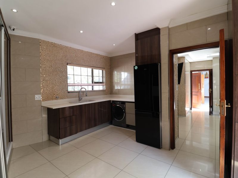 Modern kitchen featuring dark wood cabinetry, stone countertops, tiled backsplash, and integrated appliances with neutral porcelain floor tiles.