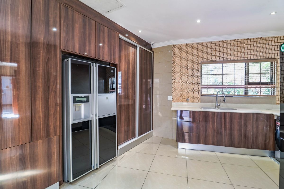 Modern kitchen featuring high-gloss wood-finish cabinetry, stone countertops, a mosaic tile backsplash, and integrated appliances with neutral floor tiling.