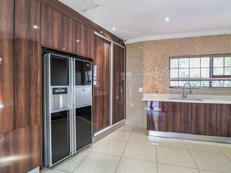 Modern kitchen featuring high-gloss wood-finish cabinetry, stone countertops, a mosaic tile backsplash, and integrated appliances with neutral floor tiling.
