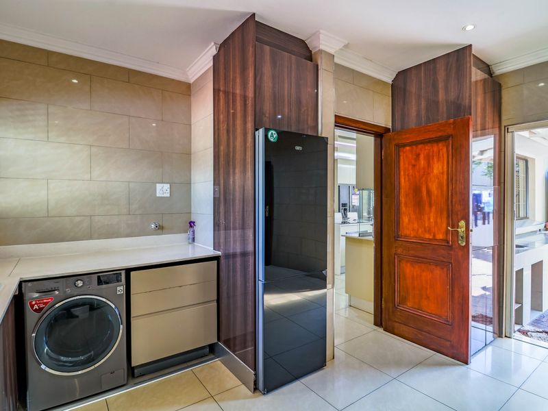 A functional scullery featuring modern built-in cabinetry, stone countertops, tiled splashbacks, and tiled flooring, providing convenient access to the kitchen and outdoor area.