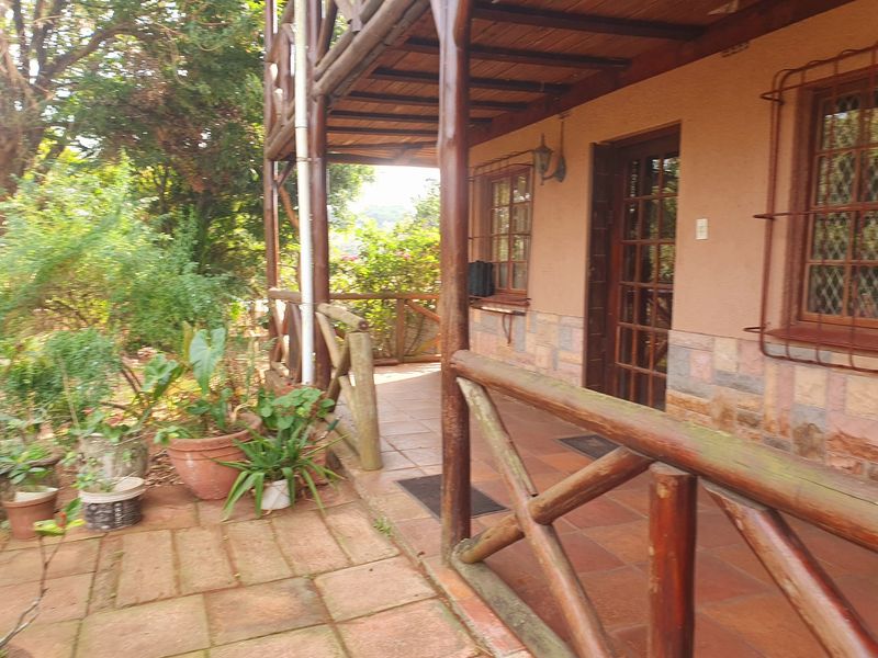 A covered outdoor patio area featuring timber structural elements, tiled flooring, and stone cladding, providing access to the home through a timber-framed glass door.
