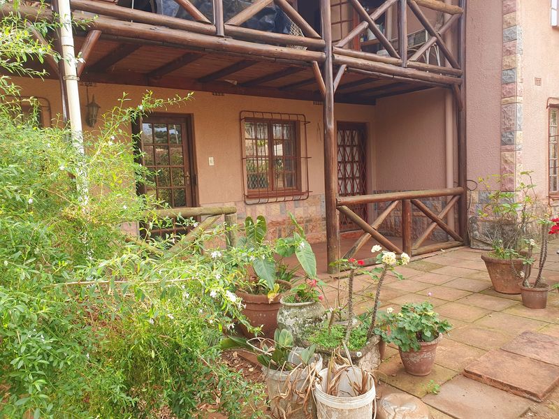 A covered ground-floor patio area featuring timber railings, stone-clad accents, and direct access to the home through timber-framed doors.