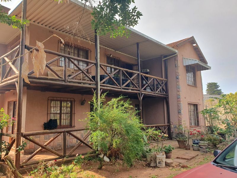 Two-story residential exterior featuring a timber balcony, covered patio area, and security-fitted windows with stone cladding accents.