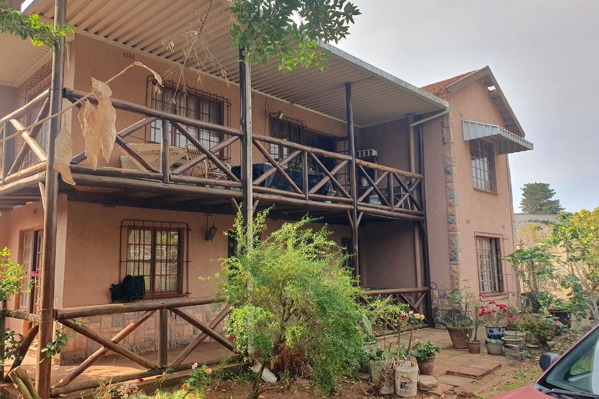 Two-story residential exterior featuring a timber balcony, covered patio area, and security-fitted windows with stone cladding accents.