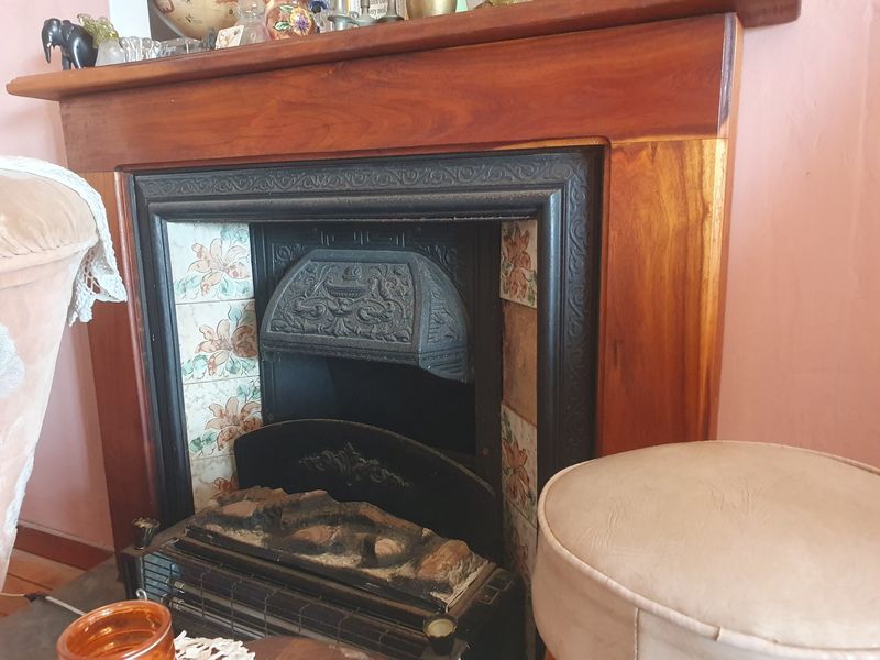 A classic living room feature fireplace with a timber mantel, cast iron insert, and decorative floral ceramic tiles.