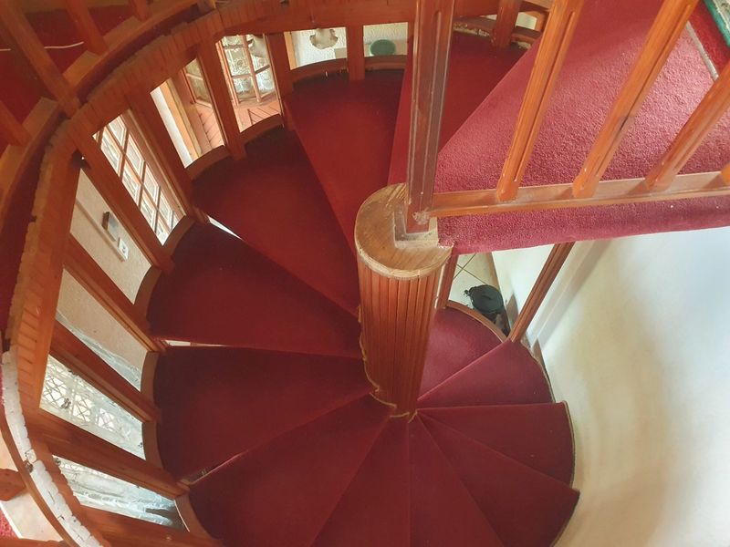 A spiral staircase featuring a wooden balustrade and red carpeted treads, providing a central architectural feature within the home.