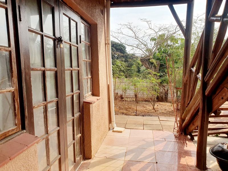 A covered patio area featuring tiled flooring and timber-framed glass doors, leading out to a garden space.