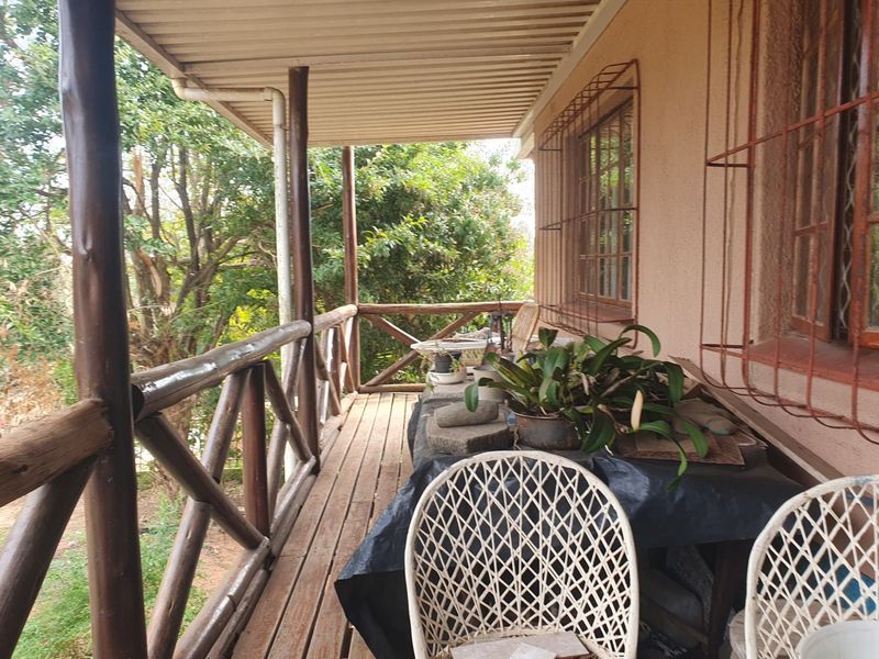 A covered timber balcony featuring wooden railings and support posts, overlooking a garden area with metal security bars on the windows.