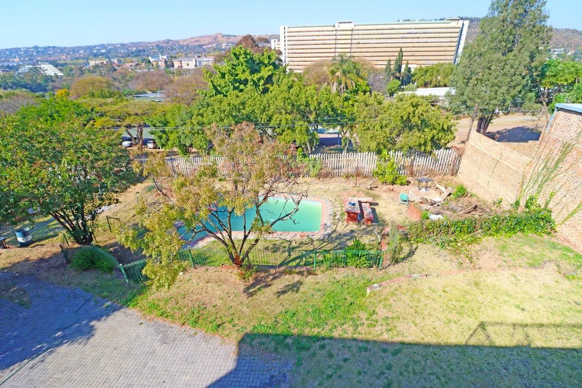 Aerial view of a residential backyard featuring a swimming pool, paved area, and perimeter fencing, set against an urban landscape.