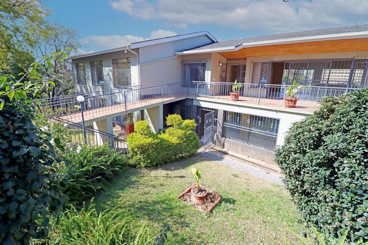 Rear view of the property featuring a raised walkway, balcony with timber soffit, and a lower paved patio area with security bars.