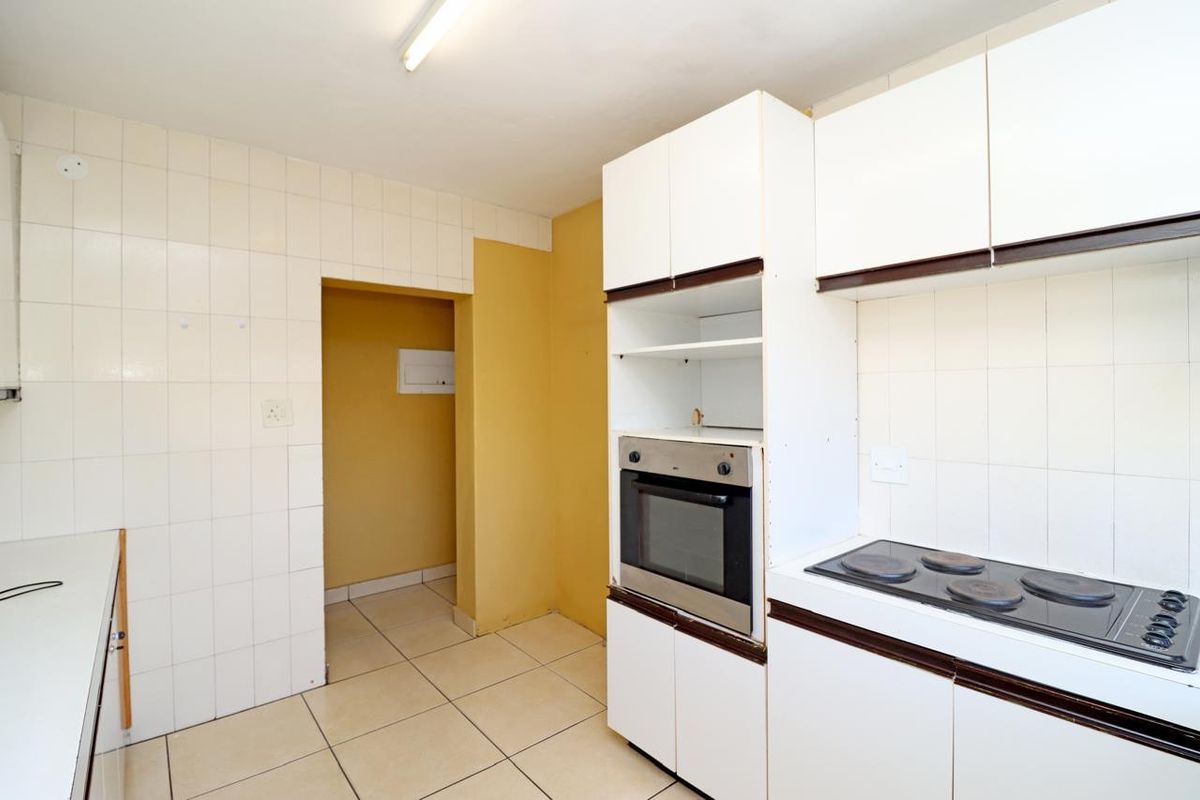 A functional kitchen featuring built-in cabinetry, an integrated oven, and an electric hob, with tiled splashbacks and flooring throughout.