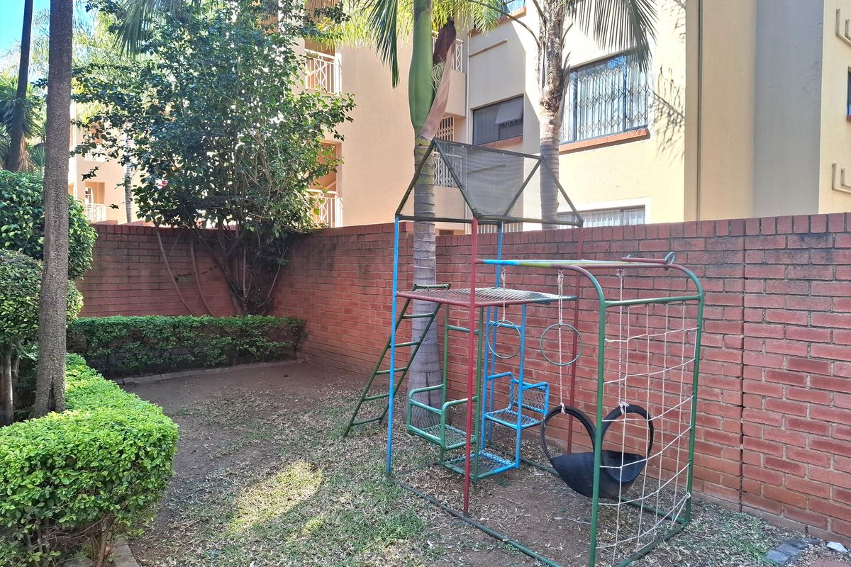 A private rear garden area featuring a brick boundary wall, established landscaping, and mature palm trees.