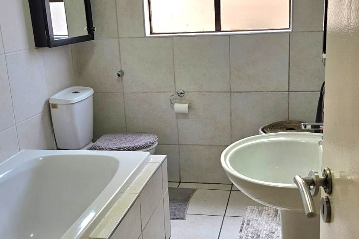 A functional bathroom featuring a bathtub, pedestal basin, and toilet, finished with neutral wall and floor tiles.