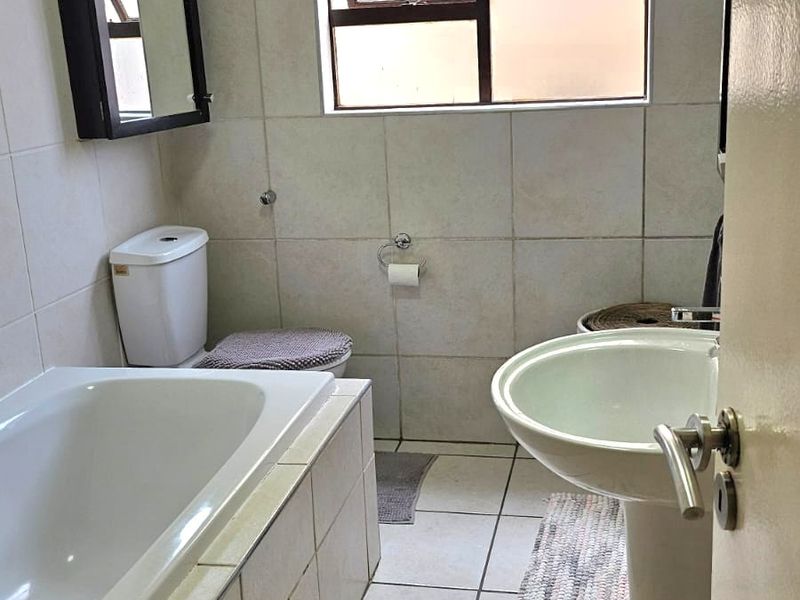 A functional bathroom featuring a bathtub, pedestal basin, and toilet, finished with neutral wall and floor tiles.