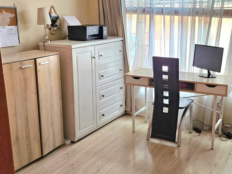 A functional home office space featuring light-toned laminate flooring, neutral wall finishes, and a large window with curtain treatments.