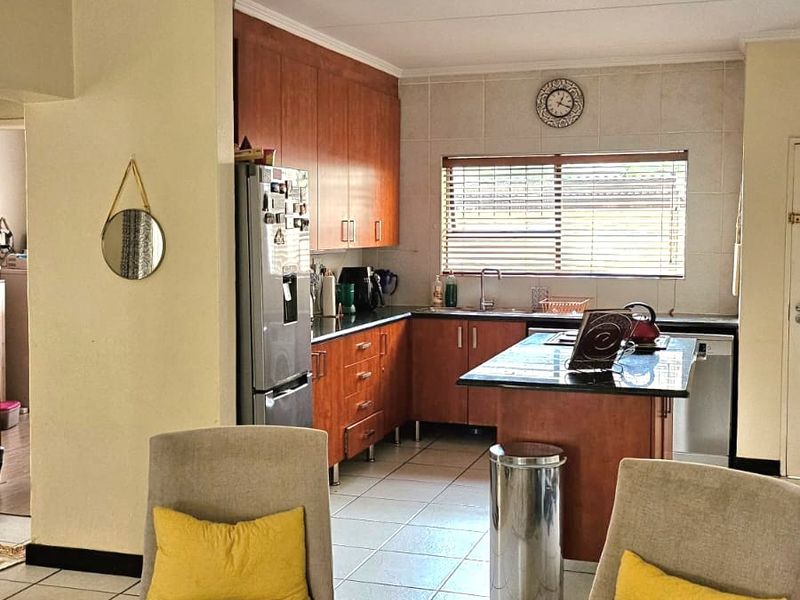 Open plan kitchen featuring wooden cabinetry, granite countertops, and a central island, seamlessly flowing into the adjacent living area with tiled flooring throughout.