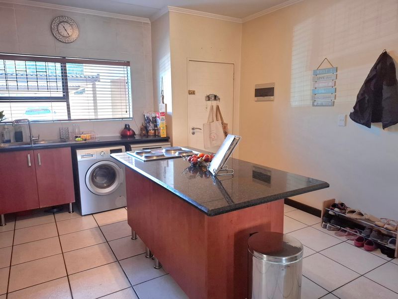 A functional kitchen featuring a central island with a built-in hob, granite countertops, tiled flooring, and ample under-counter storage space.
