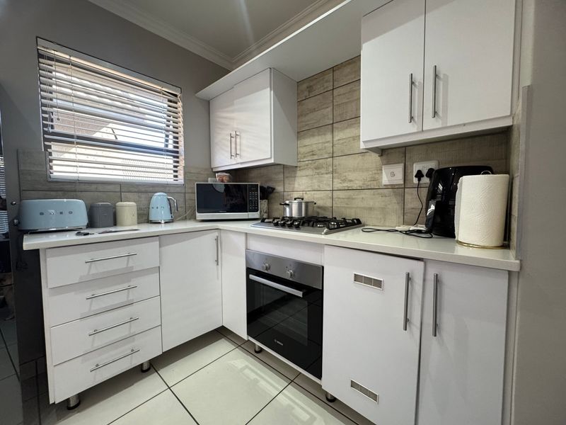 A modern, well-maintained kitchen featuring white cabinetry, stone countertops, a gas hob, and a tiled backsplash with neutral tones.