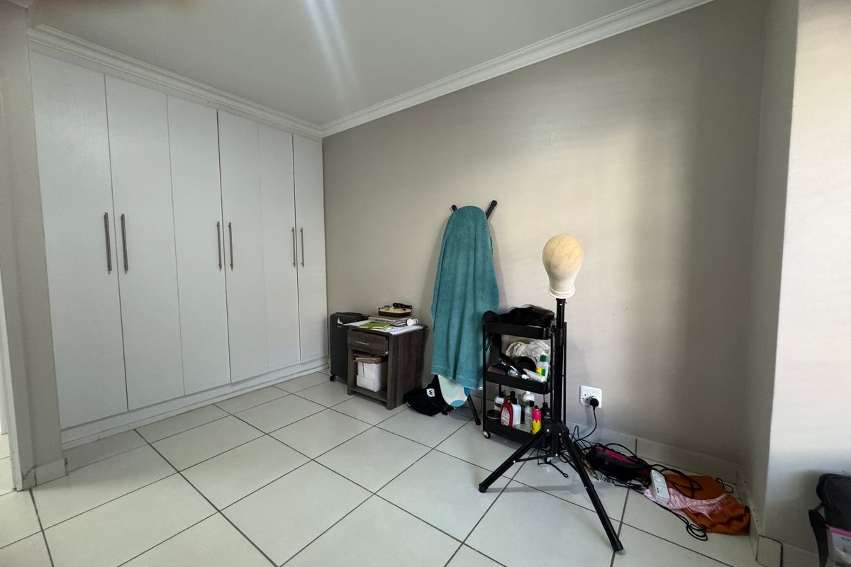 A bedroom featuring neutral wall paint, tiled flooring, and extensive white built-in cupboards providing ample storage space.