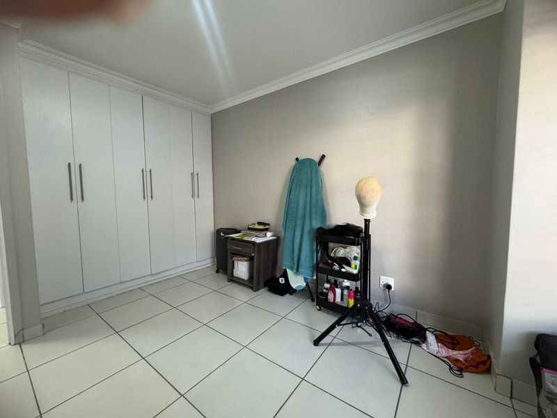 A bedroom featuring neutral wall paint, tiled flooring, and extensive white built-in cupboards providing ample storage space.