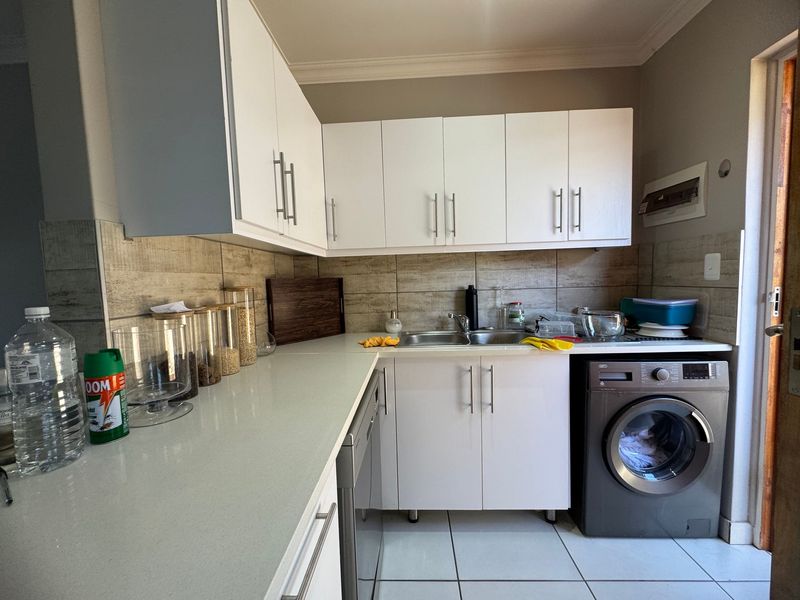 A functional kitchen featuring white cabinetry, stone countertops, a stainless steel sink, tiled backsplash, and a built-in washing machine.
