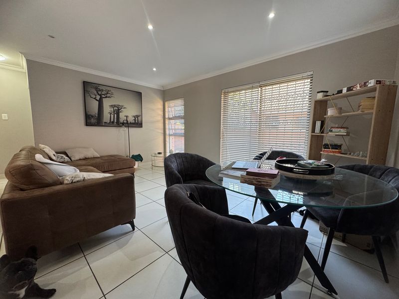 An open-plan living and dining area featuring neutral tiled flooring, recessed downlighting, and large windows fitted with venetian blinds.