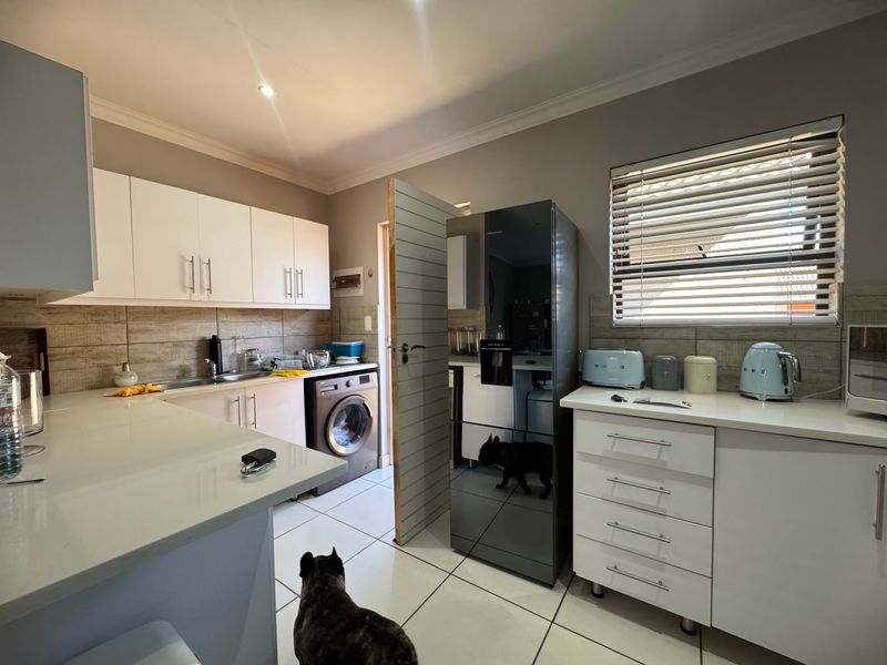 A functional kitchen featuring white cabinetry, stone countertops, tiled backsplash, and integrated laundry facilities, offering a clean and practical workspace.