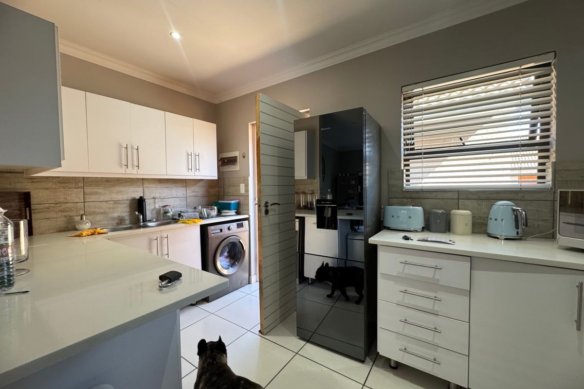 A functional kitchen featuring white cabinetry, stone countertops, tiled backsplash, and integrated laundry facilities, offering a clean and practical workspace.
