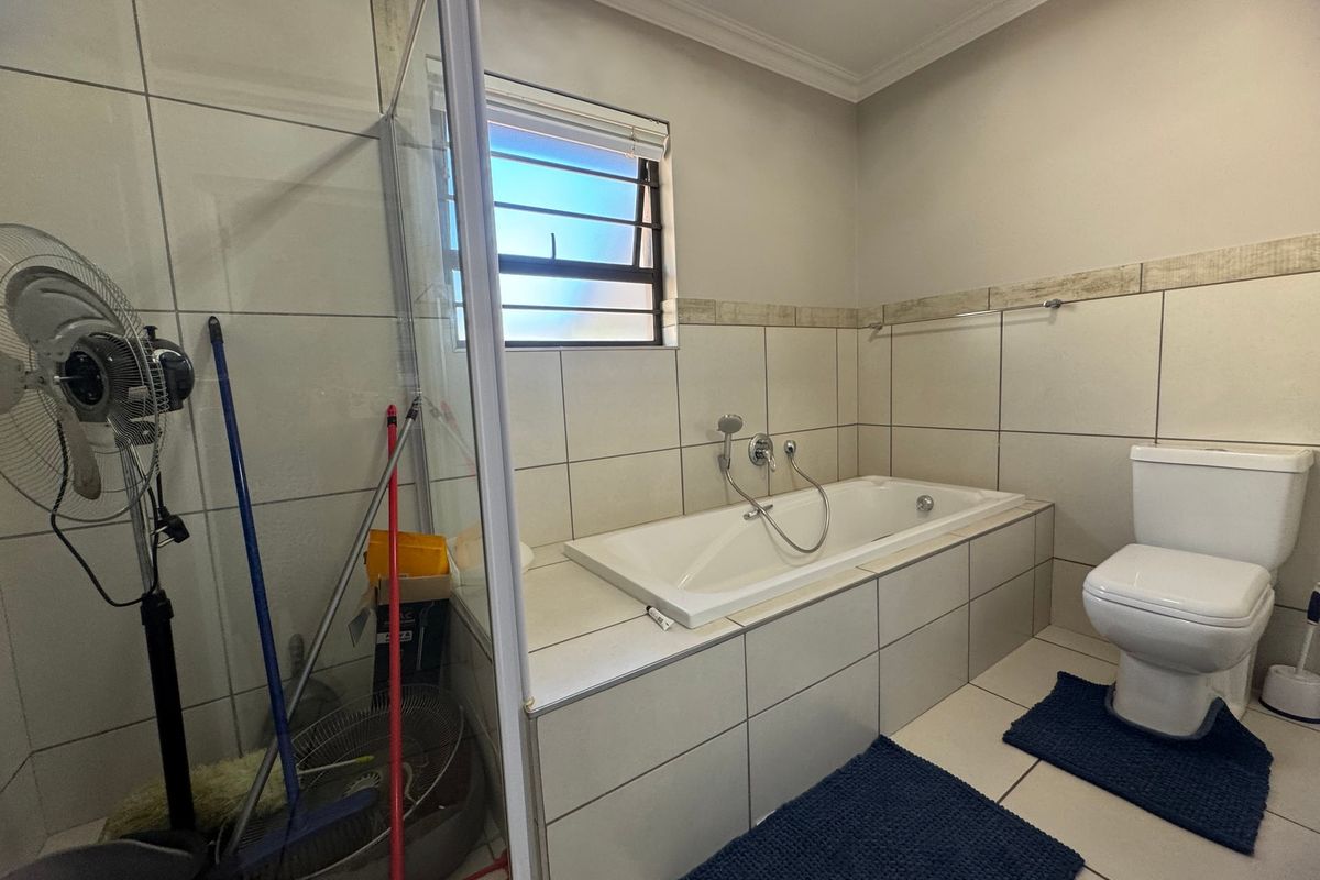 A functional bathroom featuring a built-in bathtub, separate shower enclosure, and toilet with neutral wall and floor tiling.