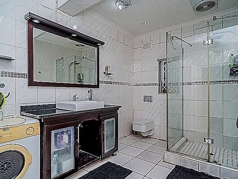 A functional bathroom featuring a vanity with a vessel sink, a glass-enclosed shower, and a wall-hung toilet, finished with tiled surfaces throughout.